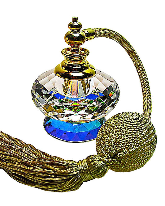 A faceted clear glass perfume bottle with a blue iridescent base, topped with a gold cap and connected to a long gold cord with a tassel and round tassel bead, photographed on a plain light background.