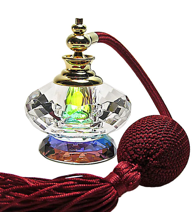 A faceted clear glass perfume bottle with a gold-toned cap, filled with iridescent liquid, attached to a deep red silk cord and tassel, photographed on a white background.