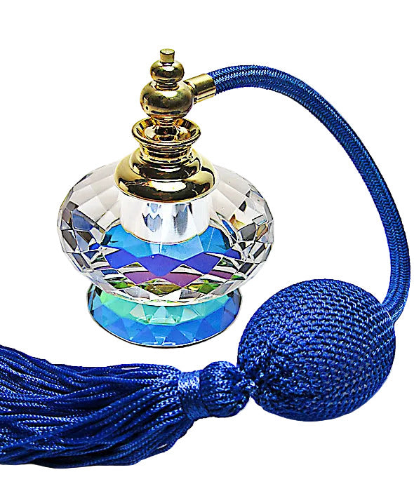 A faceted clear glass perfume bottle with a gold-toned cap, a blue iridescent interior, and a long blue tassel with a round blue bead, photographed on a white background.