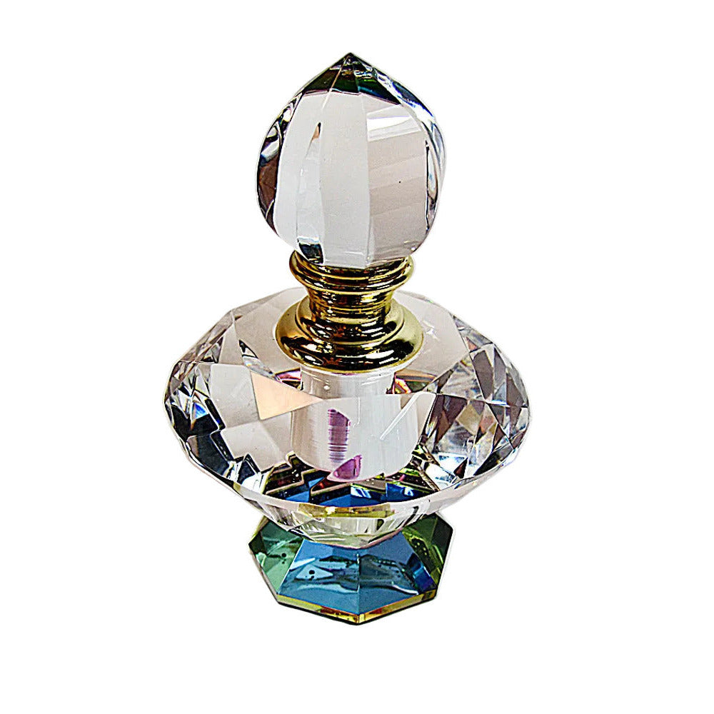 A clear faceted crystal perfume bottle with a matching crystal stopper, a gold-tone collar, and a small iridescent blue-green base, photographed on a plain light background.