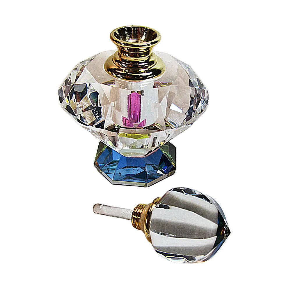A clear faceted perfume bottle with a blue base and gold neck, shown with its matching clear cap placed in front on a white background.