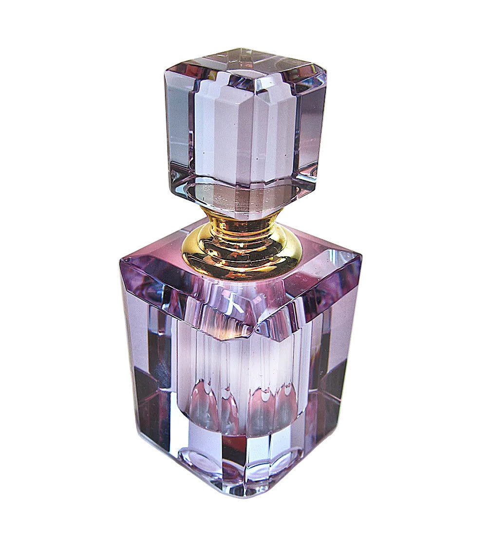 A faceted crystal perfume bottle with a matching stopper, featuring a translucent lavender-purple body and a polished gold neck collar, set against a plain white background.